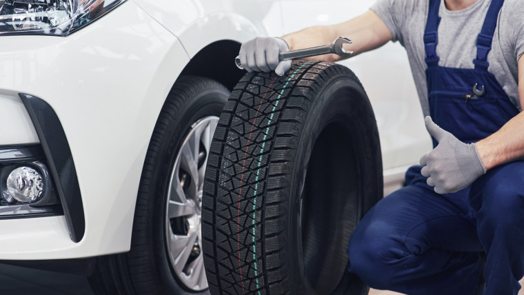 technician with blue workwear holding wrench tire while showing thumb up