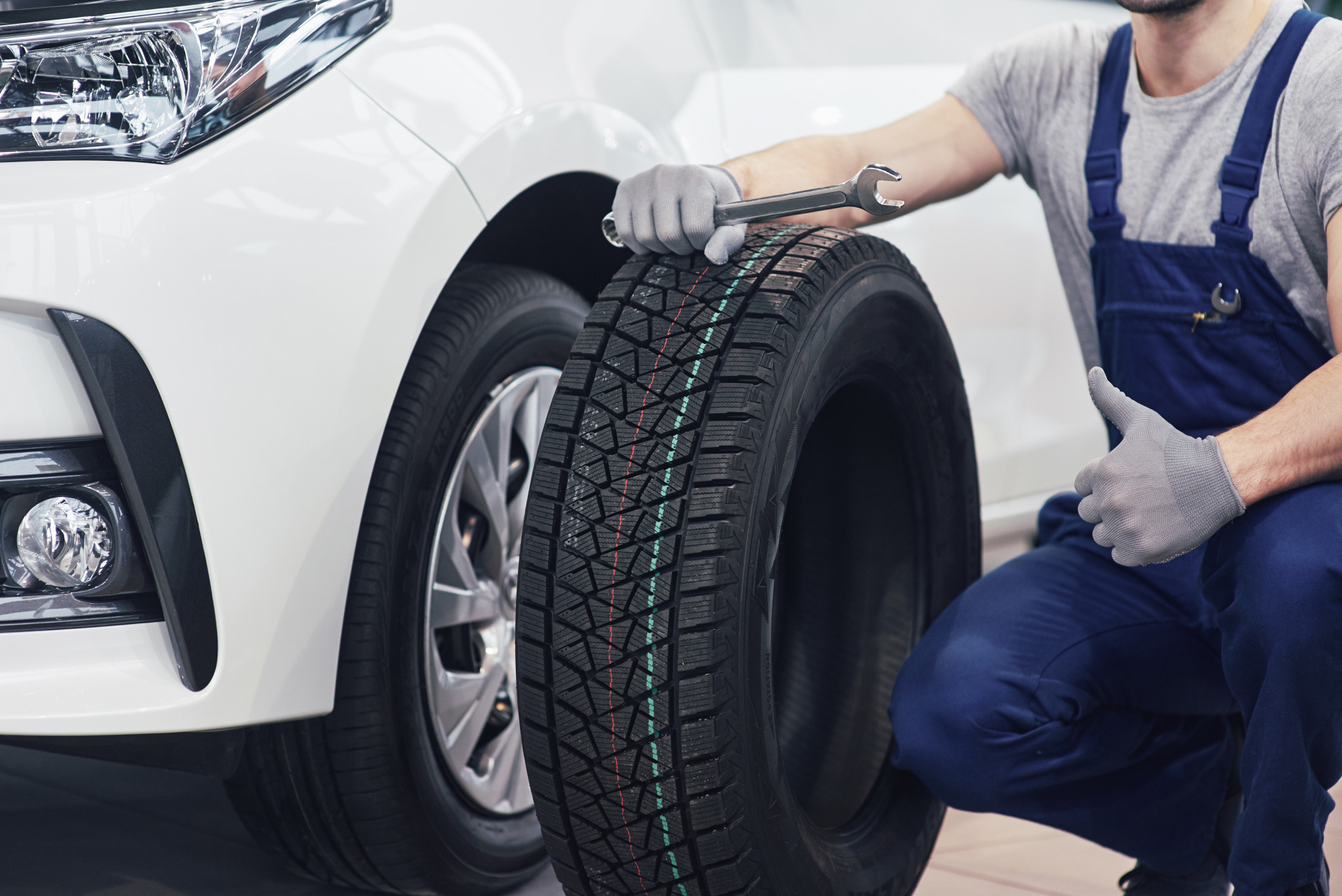 technician with blue workwear holding wrench tire while showing thumb up